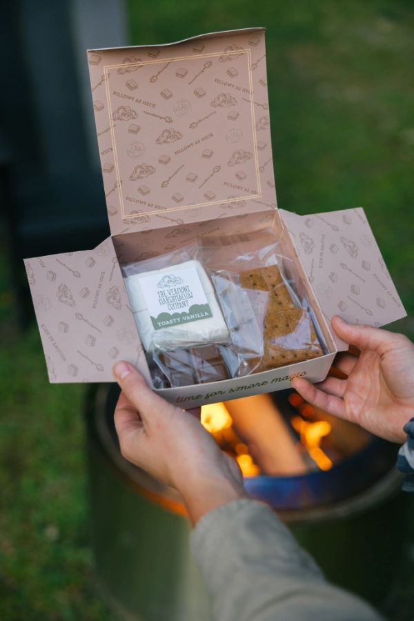 Hands holding a welcome gift box with snacks near an outdoor fire